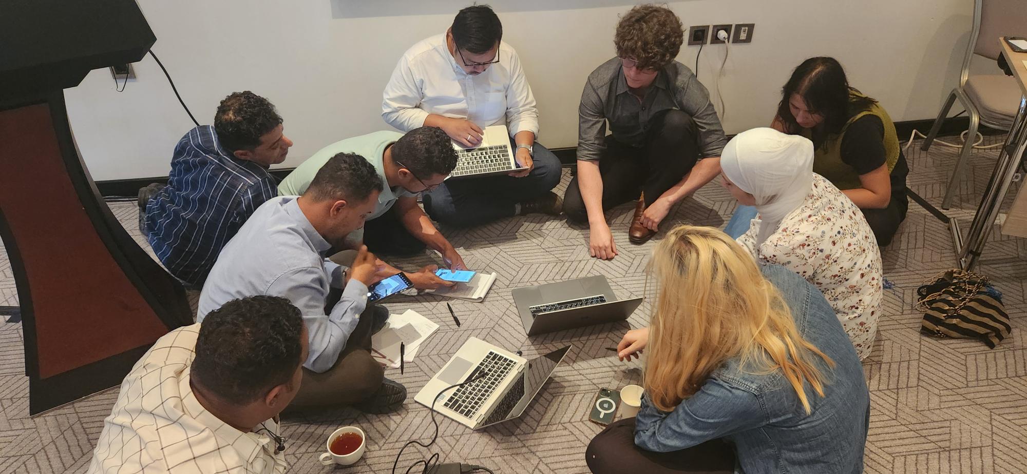A group of people sitting on the floor in a room collaborate on a group activity. 