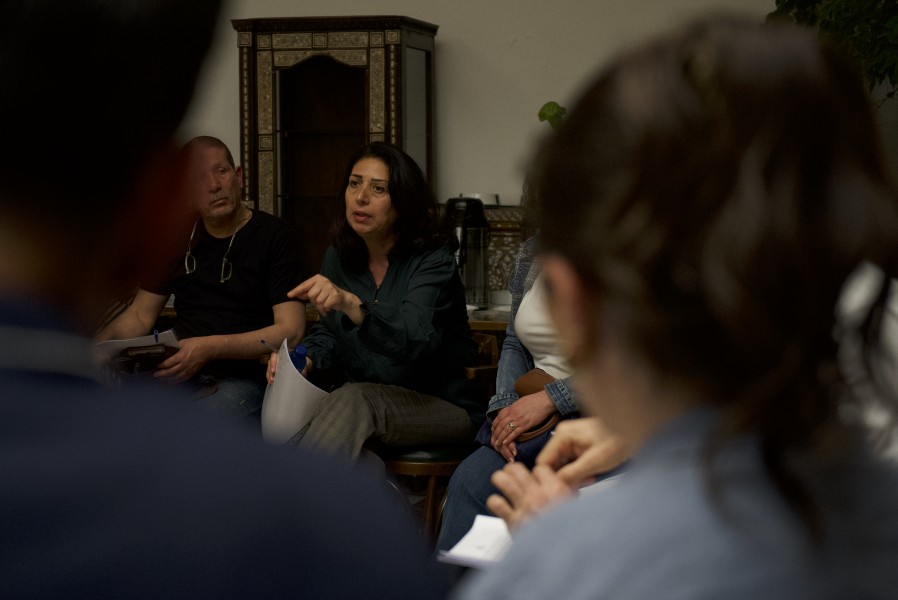A woman seated in a chair gestures as she speaks to others seated around in a circle.