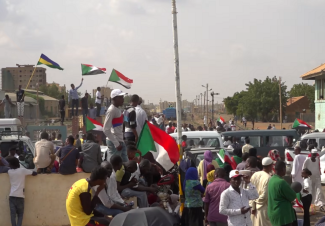 People gather in front of government buildings in Khartoum waiving Sudanese flags.