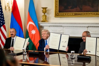 Armenian Prime Minister, Azerbaijani President, and U.S. President, seated at a table and wearing suits, each hold up a signed document in their hands
