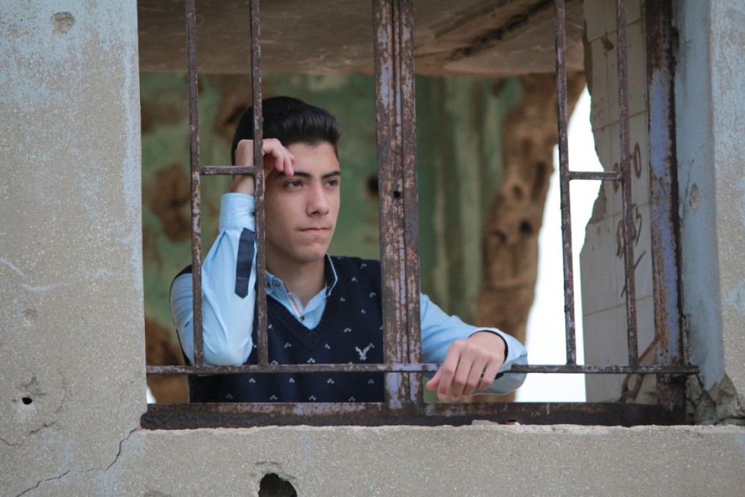Image of a Lebanese teenager looking into the horizon through a window of a war-wrecked building
