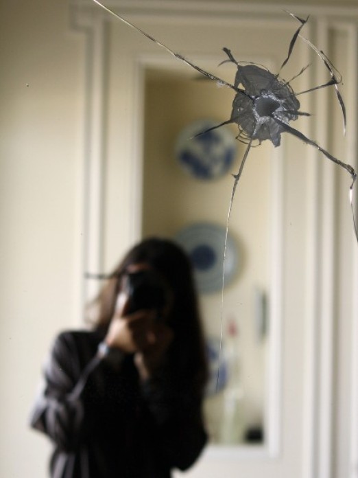 Image of a dining room mirror with a bullet hole in it, and a faded reflection of the young woman photographer