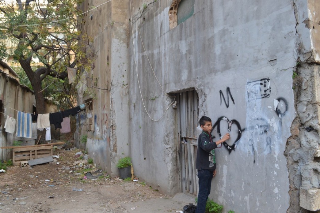Image of a child scribbling on a wall of house that witness Lebanese civil war with many bullet holes
