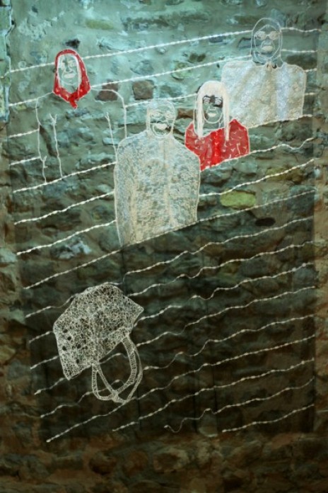 A piece of textile art, where the artist has embroidered four people at the top and an upside down koffa basket near the bottom, on a piece of transparent tulle.